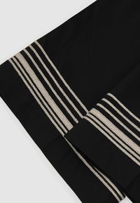 Tissu noir avec plusieurs bandes parallèles beiges brodées le long des bords, plié sur un fond clair.