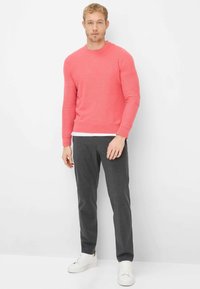 Korallenroter Strickpullover mit langen Ärmeln und rundem Ausschnitt, kombiniert mit dunkelgrauer Hose und weißen Sneakers. Einfaches, klares Design.