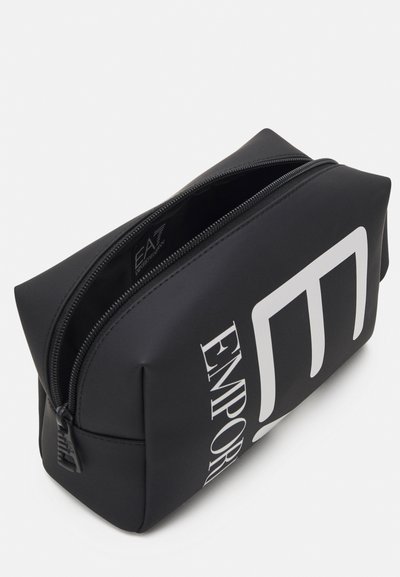 Trousse de maquillage noire en matériau lisse, dotée d'une fermeture éclair. L'avant présente un grand texte blanc "EMPORIO" et un logo.