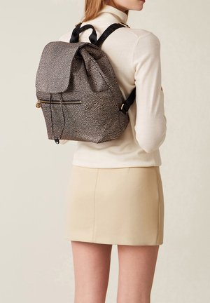 Zaino in tessuto a pois bianchi e neri con patta pieghevole, chiusura con coulisse e tasca frontale con zip; spallacci regolabili.