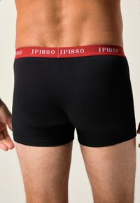 Černé boxerky vyrobené z bavlny, s červeným elastickým pasem s potiskem "JP1880". Přiléhavý design zvýrazňuje tvar těla.
