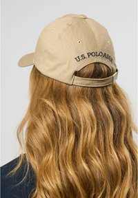 Beige cap with a curved brim, made of cotton, featuring "U.S. POLO ASSN." embroidered on the back. Adjustable strap visible at the back.