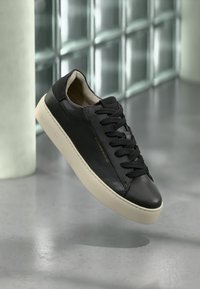 Sneaker in pelle nera con finitura liscia e design dei lacci in tonalità. Presenta una suola in gomma crema e un dettaglio di branding minimalista.