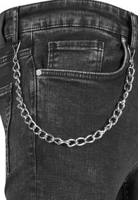 Chaîne en argent attachée aux passants de ceinture d'un jean en denim noir, drapée sur la poche latérale.