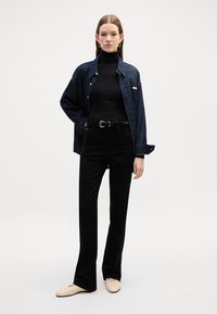 Tamni traper košulja preko crnog turtleneck-a, uparena s hlačama s visokim strukom i crnim zvonastim krojem te bež cipelama na slip-on. Ovaj look dodatno naglašava crni remen.