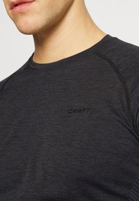 Dunkelgraues Kurzarm-T-Shirt aus strukturiertem Stoff, mit einem dezenten schwarzen Logo auf der Brust und flachen Nahtdetails.