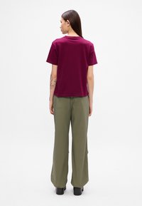 Μαρόν βαμβακερό t-shirt με άνετη εφαρμογή, κοντά μανίκια και στρογγυλή λαιμόκοψη, συνδυασμένο με φαρδιά ελαιόχρωμα παντελόνια και μαύρες πλατφόρμες.