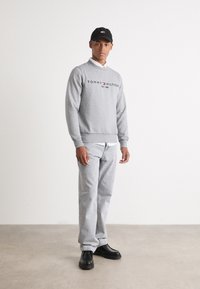 Pelēks džemperis ar "TOMMY HILFIGER" logo, apvienots ar gaiši pelēkām biksēm un melnām kurpēm. Melns cepure ar logo priekšpusē. Vienkāršs dizains.