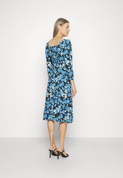 Φλοράλ φόρεμα με μοτίβο σε μαύρο και μπλε χρώμα, με σμιχτό πίσω μέρος, τρία τέταρτα μανίκια, μέχρι το γόνατο, συνδυασμένο με μαύρες ανοιχτές γόβες.