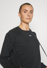 Sudadera negra con cuello redondo y puños de canalé. Presenta un pequeño logo en el pecho y una textura suave.