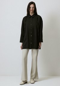 Black long-sleeve shirt with a buttoned front, featuring a collar and slight sheen; paired with cream wide-leg trousers, and light shoes.