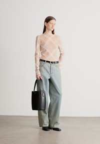 Bluză bej cu mâneci lungi și model în formă de romb, blugi evazați albastru deschis, curea neagră, geantă tote neagră și pantofi negri comozi. Fundal simplu.