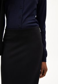 Navy gebreide shirt met knoopsluiting aan de voorkant en lange mouwen, gecombineerd met een eenvoudige zwarte pencilrok. Gladde stof, getailleerde pasvorm.
