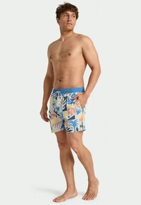 Peldbikses ar zilu elastīgu jostu, zilu, oranžu un dzeltenu tropisko rakstu sajaukumu un ar auklas aizdari.