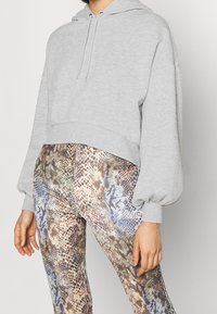 Felpa grigia corta con cappuccio regolabile e maniche a palloncino abbinata a leggings con un motivo in pelle di serpente multicolore.