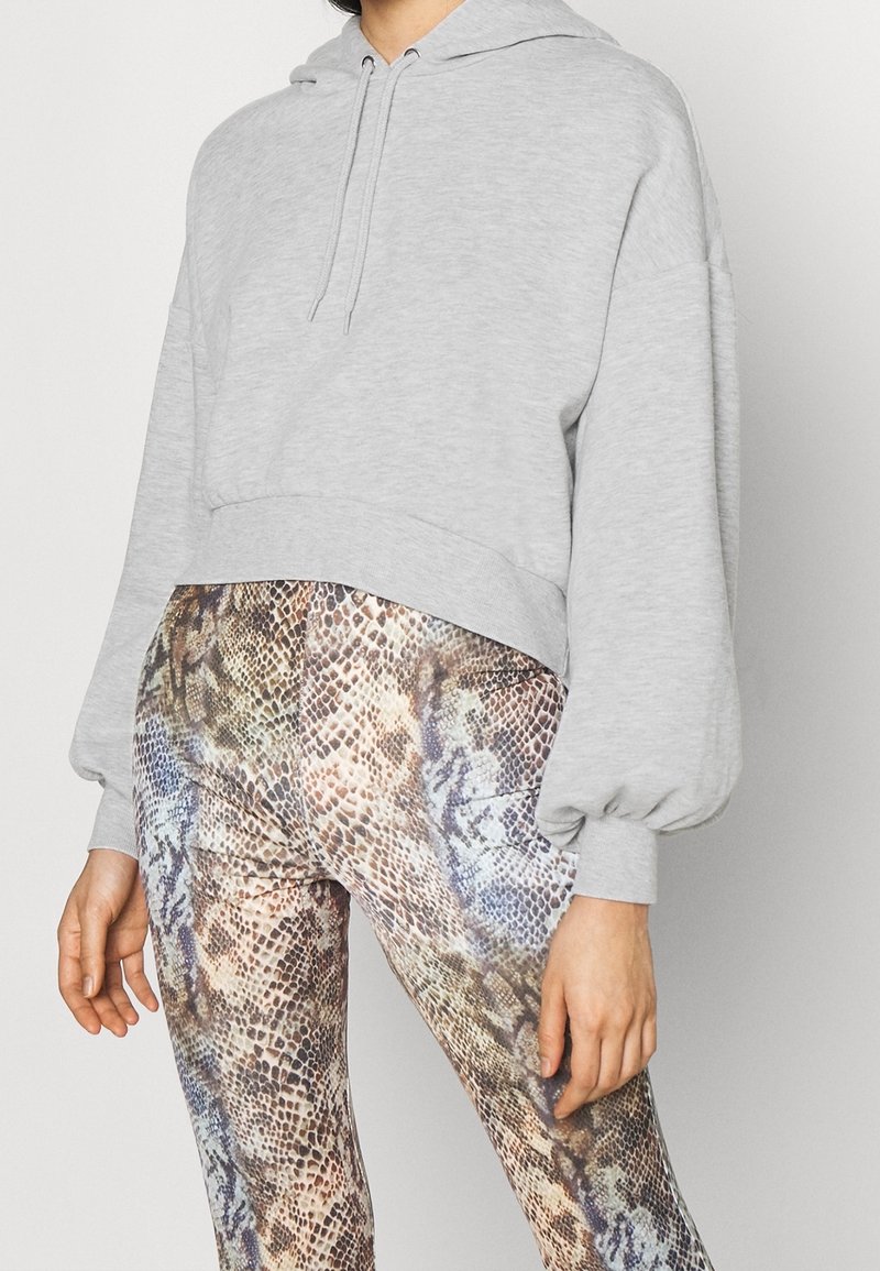 Felpa grigia corta con cappuccio regolabile e maniche a palloncino abbinata a leggings con un motivo in pelle di serpente multicolore.