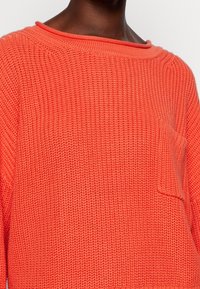 Jasně korálový pletený svetr s volným střihem, širokým výstřihem a přední kapsou. Texturovaná látka s žebrovaným vzorem.