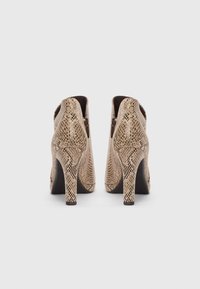 Bottines à imprimé serpent beiges avec une finition texturée, dotées d'un talon haut et de fermetures éclair sur le côté.