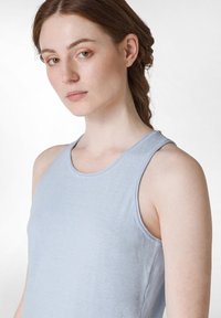 Světle modrý tílko vyrobené z jemné látky, s bezrukávovým designem, kulatým výstřihem a mírně texturovaným povrchem.