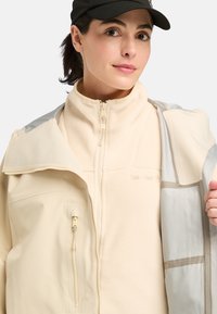 Lichtbeige zip-up jas met een fleece binnenlaag, contrasterende glanzende stof op de schouders en een borstzak met een ritsdetail.