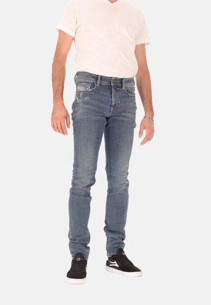 Jeans da uomo a taglio slim in denim blu chiaro, con effetto usurato frontale, design standard con cinque tasche e abbinati a sneakers nere.