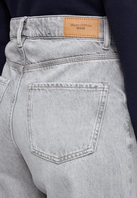 Sivé rifľové nohavice s vysokým pásom, zadnými vreckami a koženou značkou s nápisom "Marc O'Polo DENIM" na zadnej strane. Textúrovaný povrch.