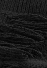 Gros plan d'un tissu tricoté noir avec un fil épais et des pampilles à franges, montrant une texture détaillée et un motif de tissage.