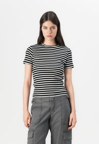 T-shirt de riscas pretas e brancas com textura canelada e decote redondo, combinado com calças cargo cinzentas com bolsos laterais e um corte descontraído.