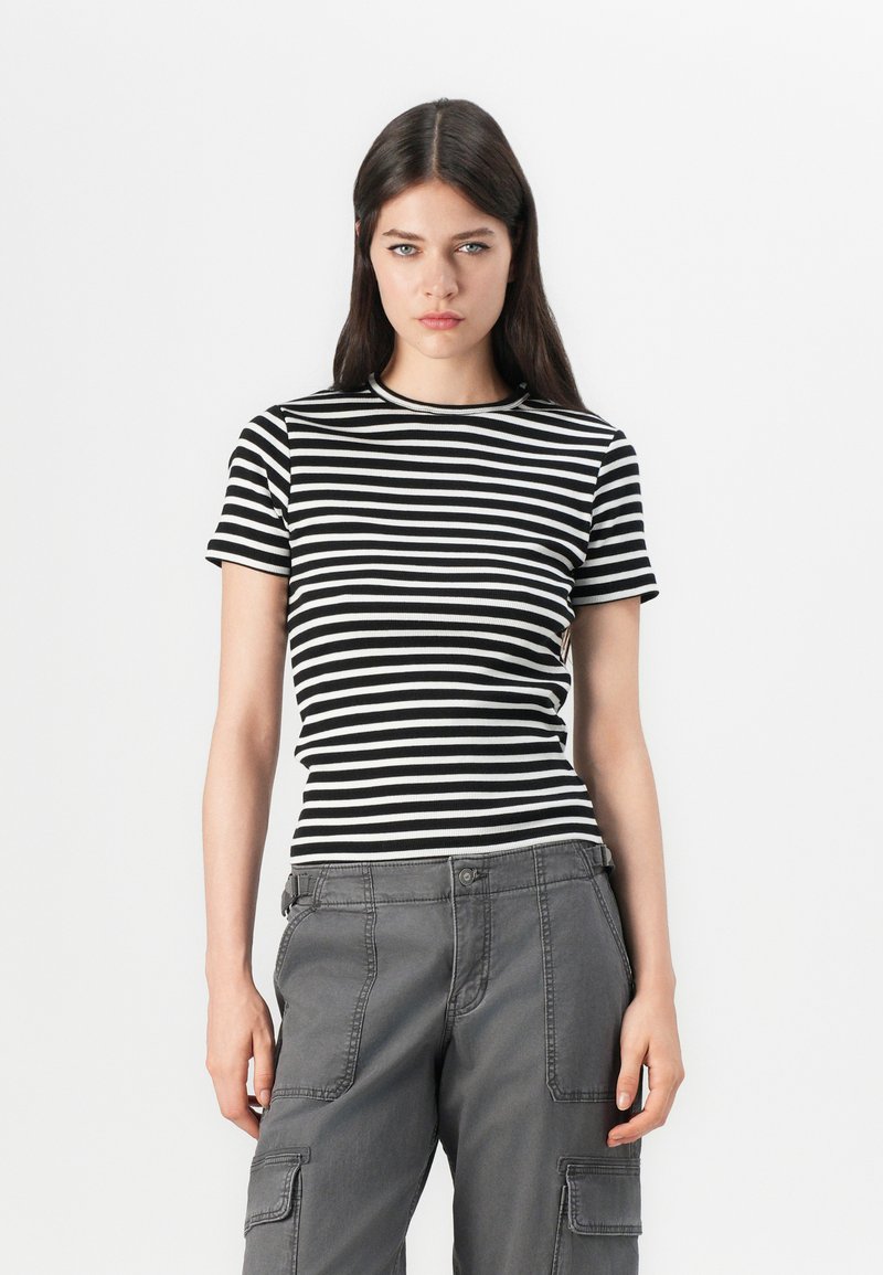 Black and white striped t-shirt with a ribbed texture and crew neckline, paired with gray cargo pants featuring side pockets and a relaxed fit.