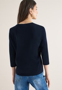 Haut bleu marine à manches trois-quarts avec un col rond, une texture lisse et une coupe décontractée, associé à un jean bleu délavé.