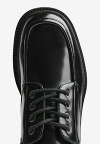 Scarpe in pelle nera con finitura liscia, punta tonda, sei fori per i lacci, laccetti neri e suola in gomma texturizzata.