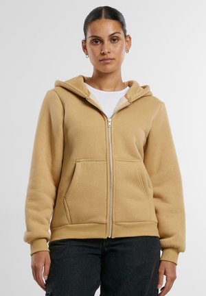 Tan zip-up hoodie made of soft material, featuring a front zipper, two pockets, and a drawstring hood. Fitted cuffs and hem.