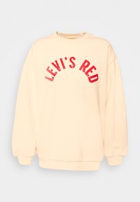 Sweatshirt de couleur crème avec col et poignets côtelés, arborant un texte en arc rouge imprimé « LEVI'S RED » sur le devant. Texture douce.