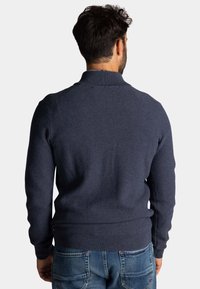 Donkerblauwe gebreide trui met een textuurpatroon, hoge kraag en geribbelde boorden en zoom, gecombineerd met lichtblauwe spijkerbroek.