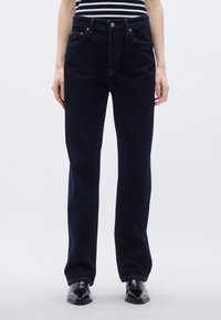 Σκούρο μπλε τζιν με ε υθείς γραμμές στα πόδια, πέντε τσέπες και αντίθετη ραφή. Διαθέτει φερμουάρ και κούμπωμα με κουμπί.