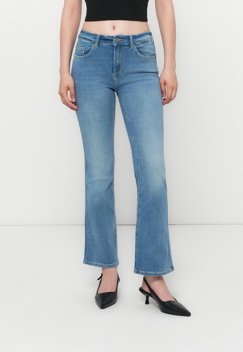 Jean flare bleu clair avec une taille mi-haute, cinq poches et des délavages subtils. Porté avec des escarpins noirs à bout pointu.