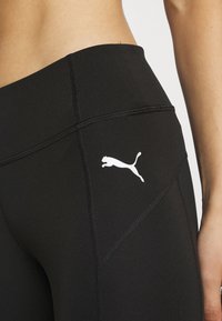 Czarne legginsy sportowe z wysokim stanem, płaskimi szwami i białym logo Pumy po lewej stronie. Gładki, elastyczny materiał o dopasowanym fasonie.