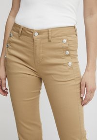 Béžové nohavice vyrobené z bavlnenej zmesi, s ozdobnými gombíkmi na bokoch, slim fit strihom a štandardnými vreckami vpredu.