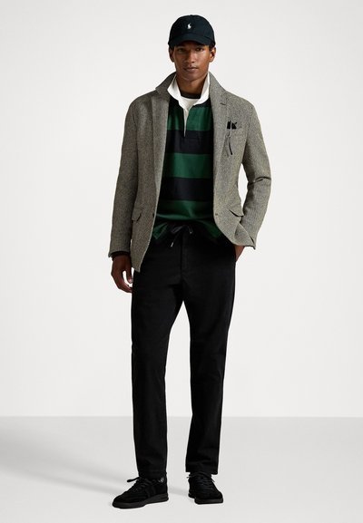 Gray houndstooth blazer over a green and black striped polo, paired with black trousers and black sneakers, finished with a black cap.