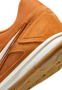 Sneaker in pelle arancione e mesh con una finitura testurizzata, caratterizzata da una suola intermedia bianca e una suola in gomma stampata etichettata "CUSHION."