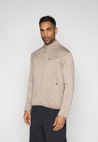 Ελαφρύ μπεζ φλις μπουφάν με ψηλό γιακά, φερμουάρ μπροστά και δύο πλαϊνές τσέπες. Διαθέτει υφή υφάσματος και διακριτικές ραφές.