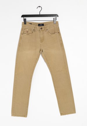 Beige slim-fit jeans met vijf zakken, hangend aan een zwarte plastic hanger tegen een witte achtergrond.