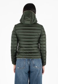 Groene pufferjack met horizontale stiksels, capuchon en elastische manchetten, gecombineerd met losse blauwe jeans op een effen achtergrond.