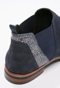 Bottine bleu marine avec panneau latéral extensible, accent de talon texturé gris argent, semelle superposée marron et languette de tirage en tissu.