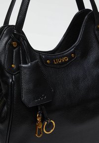Sac à main en cuir noir avec une texture granuleuse, des accents en matériel doré, une étiquette logo et des poignées doubles. Dispose d'une attache pour porte-clés.