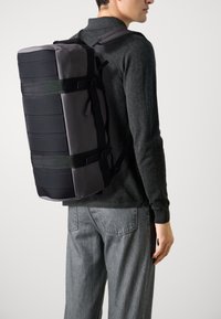 Schwarzer und grauer Rucksack mit zylindrischer Form, aus robustem Stoff gefertigt, mit verstellbaren Trägern und minimalistischen Design.