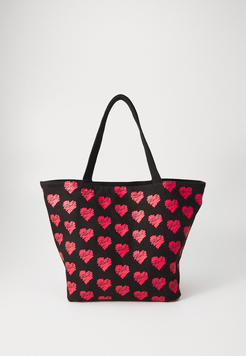 Sac fourre-tout noir avec un motif de cœurs dans des tonalités de rouge. Doté de poignées robustes et d'une forme large et structurée. Le matériau a une texture lisse.