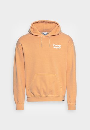 Pomarańczowa bluza z kapturem z kieszenią kangurką z przodu. Posiada regulowany kaptur oraz nadruk "Vintage Supply" na klatce piersiowej w kolorze białym. Wykonana z mieszanki bawełny.