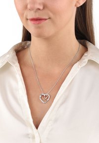 Silvrigt hjärt-halsband med en lagerdesign av hjärtan. Det yttre hjärtat har små klara ädelstenar och en slät finish. Kedjan är delikat.