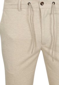 Beige gemusterde broek met een gestructureerd oppervlak, voorzien van een trekkoord in de taille en een knoopsluiting aan de voorkant.